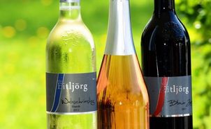 Drei Weinflaschen sind aufgereiht. Die linke Flasche ist grün, die mittlere golden und die rechte dunkel. Die Etiketten zeigen den Namen des Weinproduzenten, Ettljorg, und das Jahrgangsjahr an.