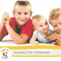 Drei junge Jungen liegen auf einem weißen Teppich. Der Junge links trägt ein rotes T-Shirt, und der Junge rechts trägt ein blaues T-Shirt. Das Baby in der Mitte trägt ein weißes T-Shirt und lächelt. Das Bild hat einen Wasserzeichen in der unteren linken Ecke.