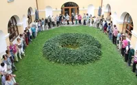 Eine Gruppe von Menschen bildet einen Kreis um einen runden Garten im Innenhof eines Gebäudes mit vielen Fenstern und gewölbten Eingängen.