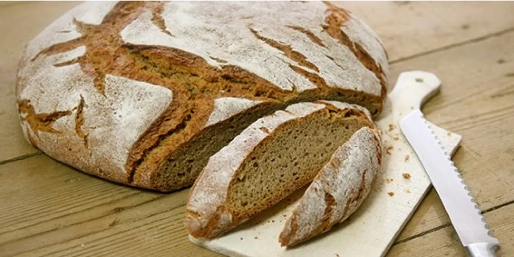 Ein ganzer Laib Brot, der in zwei Hälften geschnitten wurde, mit zwei Scheiben auf einem hölzernen Schneidebrett und einem Messer in der Nähe.