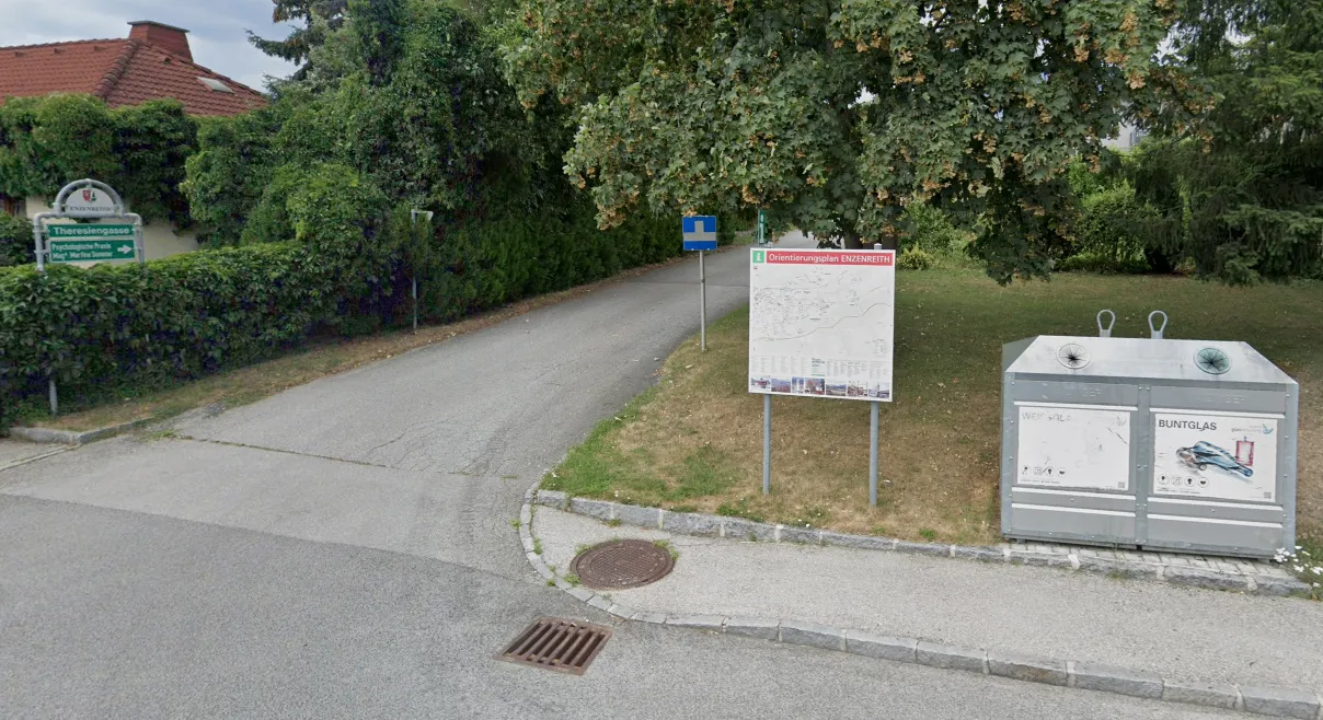 Ein Orientierungsplan auf einem Pfosten steht am Straßenrand in der Nähe eines Abwasserdeckels.