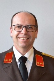 Ein Mann in Uniform mit Brille und lächelndem Gesicht. Er hat rote Sterne auf seinen Schultern.