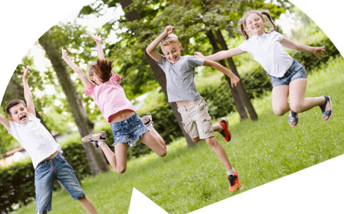 Drei Kinder springen im Gras und haben Spaß im Park. Ein Mädchen hat Zöpfe, eine andere trägt ein rosa T-Shirt und ein Junge hat Turnschuhe an.