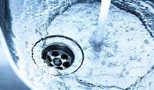 Wasser fließt aus dem Wasserhahn in ein Waschbecken und erzeugt einen wirbelnden Effekt mit Blasen. Das Waschbecken ist aus Edelstahl mit einem Abfluss.