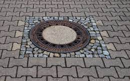 Ein Kanaldeckel mit rundem Design aus Ziegeln und Steinen auf einem Ziegelpflaster.