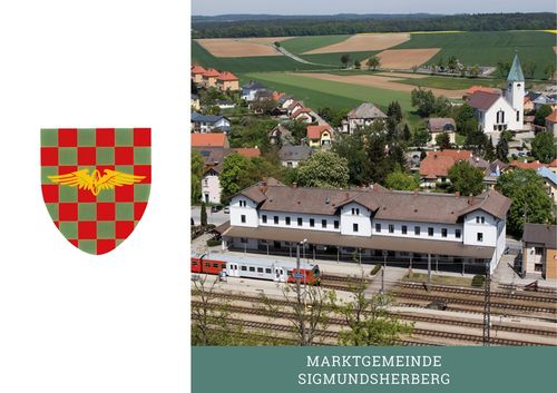 Luftaufnahme einer kleinen Stadt mit einem Bahnhof und einem Wappen auf der linken Seite.
