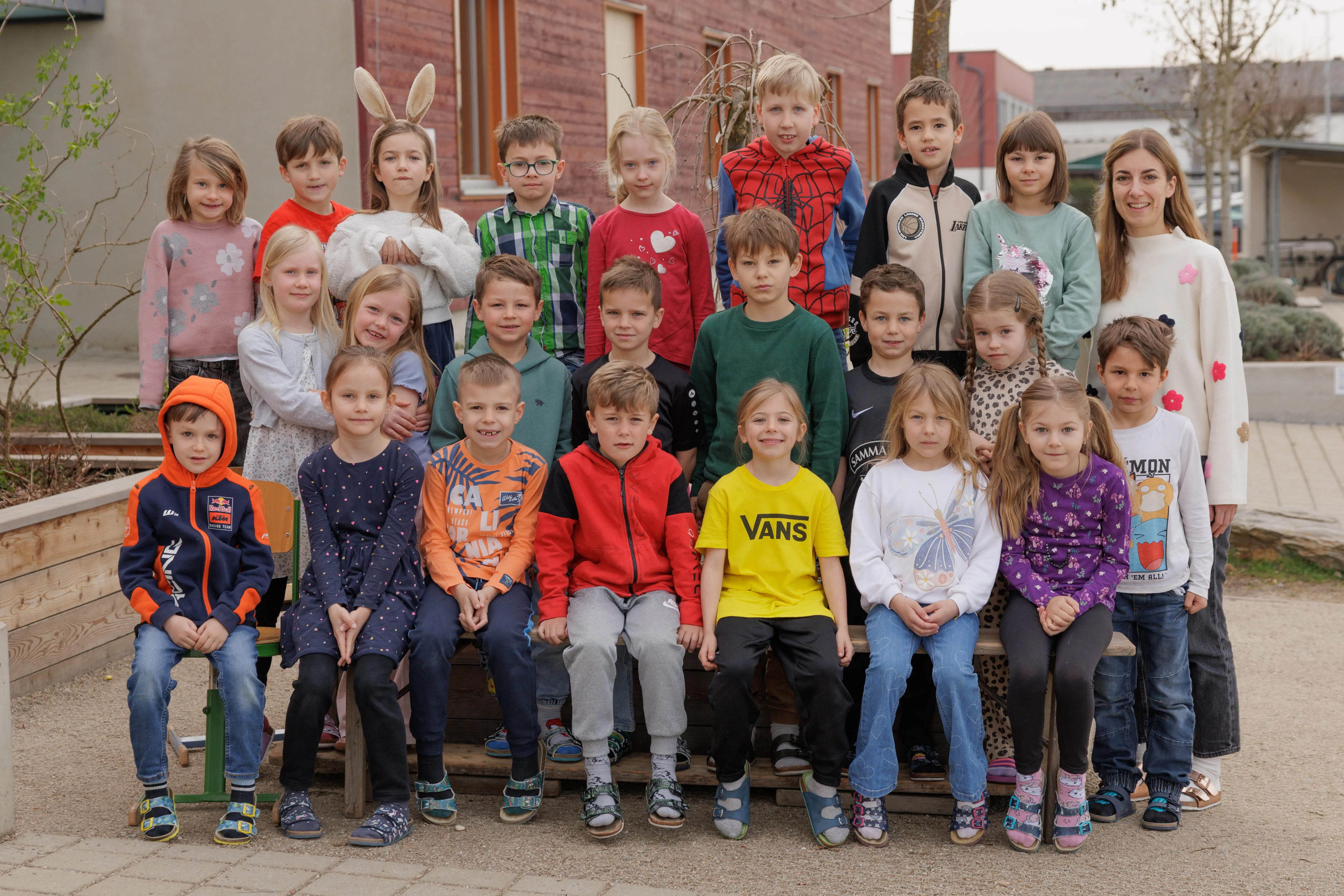 Eine Gruppe von Kindern in Freizeitkleidung posiert für ein Foto vor einem Gebäude. Einige tragen Brillen, und eines trägt Hasenohren.