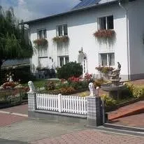 Ein großes weißes Haus mit Solarmodulen auf dem Dach, umgeben von einem Garten mit Blumen und einem weißen Zaun.