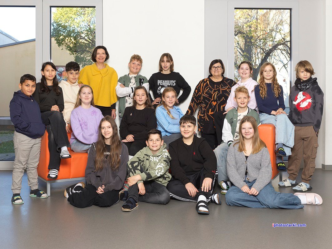 Eine Gruppe von Schülern und Lehrern posiert für ein Foto in einem Raum mit orangefarbenen Sofas und großen Fenstern.