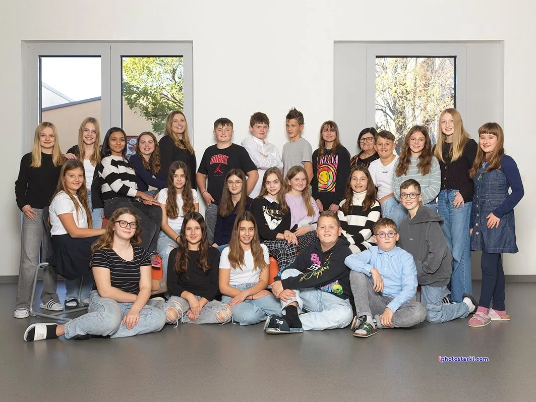 Eine Gruppe junger Menschen posiert für ein Foto. Einige von ihnen sitzen auf dem Boden, während andere hinter ihnen stehen.