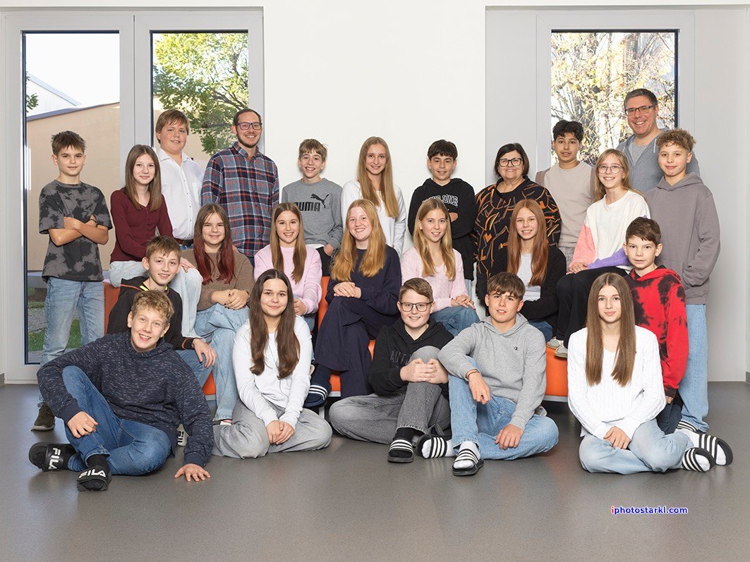 Ein Klassenfoto von Schülern und Lehrern, die für ein Bild posieren. Sie sitzen und stehen mit Lächeln im Gesicht.