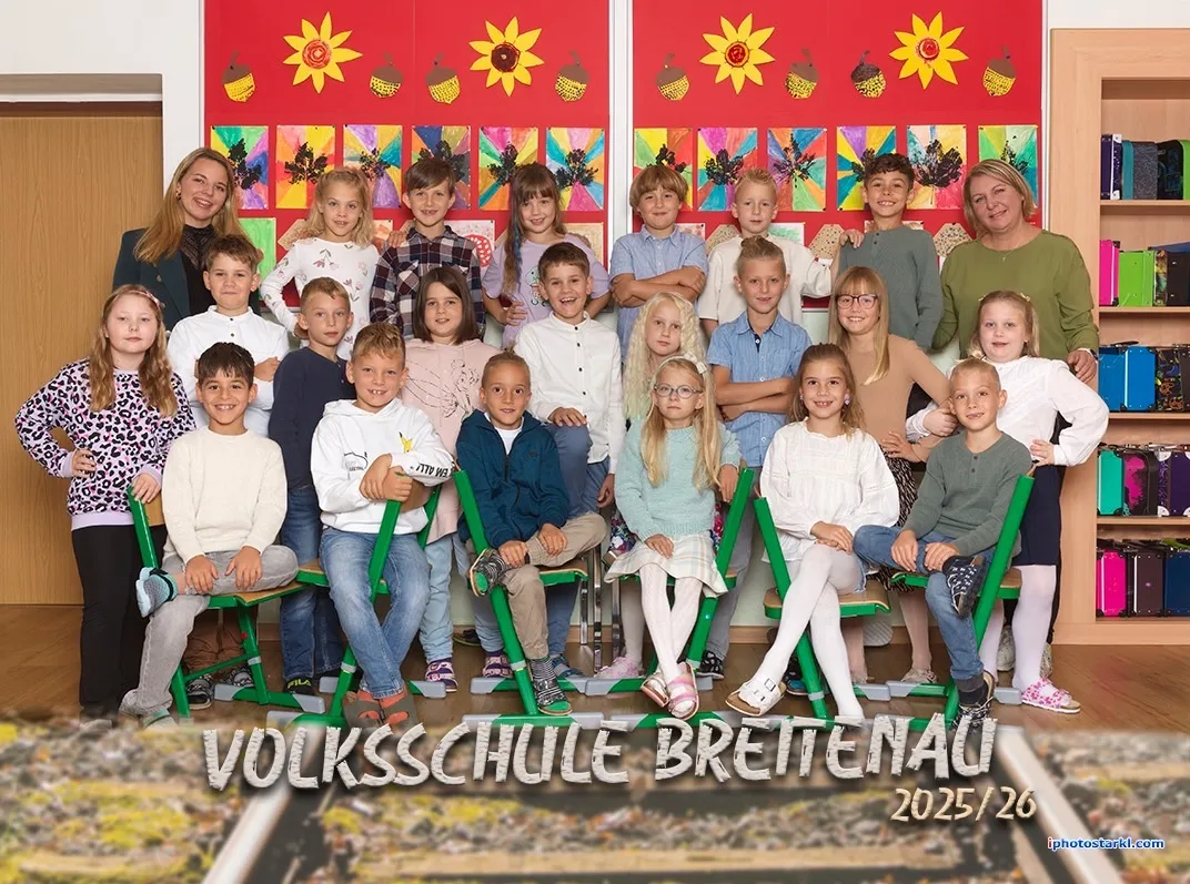 Eine Gruppe von Kindern und zwei Lehrern posiert für ein Foto im Klassenzimmer. Die Kinder sitzen auf grünen Stühlen und stehen dahinter. Das Klassenzimmer hat eine rote Wand mit Sonnenblumen und Eicheln.