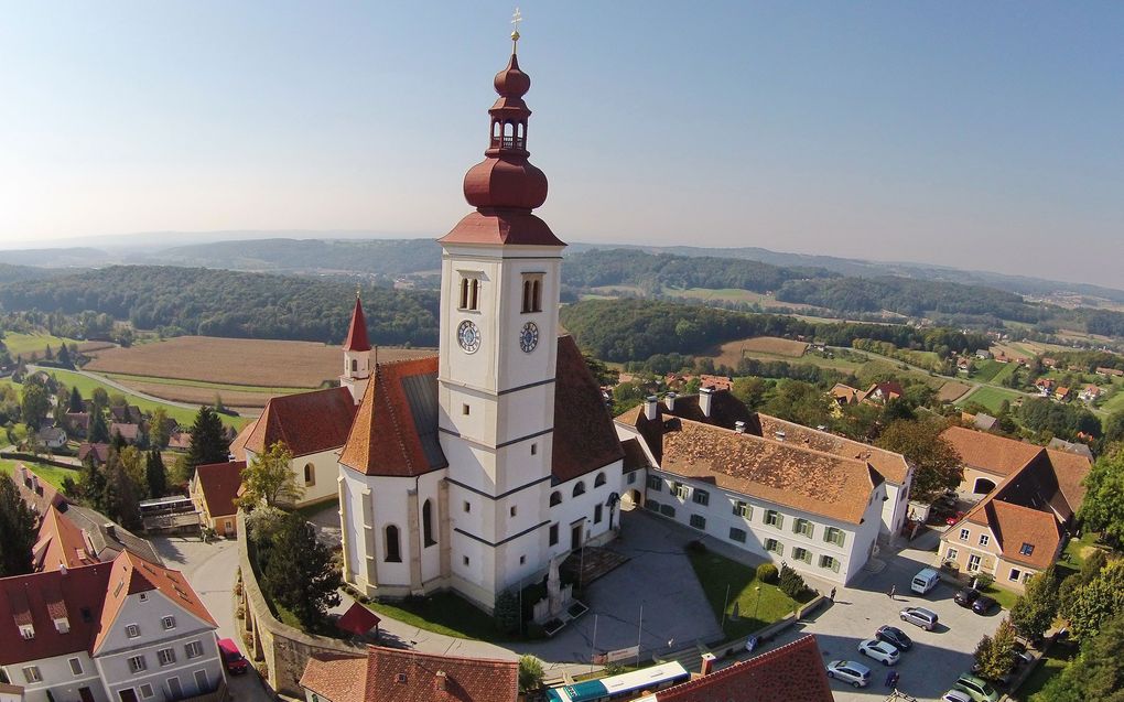Abschnittsbild: Luftaufnahme einer historischen Kirche mit hohem Turm und rotem Dach, umgeben von Gebäuden und Grünflächen.