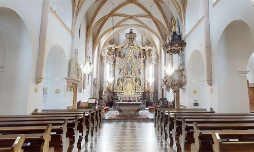 Das Innere einer Kirche mit einem goldenen Altarbild, hölzernen Kirchenbänken und einem gemusterten Boden.