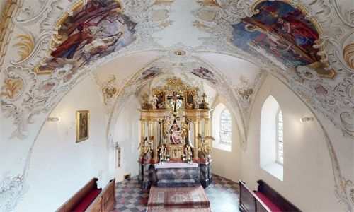 Ein kunstvoll verzierter Kapelleninnenraum mit einem goldenen Altaraufsatz, Fresken an der Decke und einem gemusterten Boden. Holzbänke sind vor dem Altar aufgestellt.