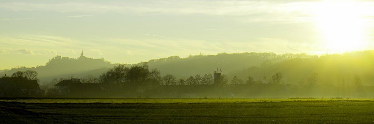 Eine friedliche Landschaft mit einem nebligen Feld, einer entfernten Stadt und einem klaren Himmel bei Morgen- oder Abenddämmerung.