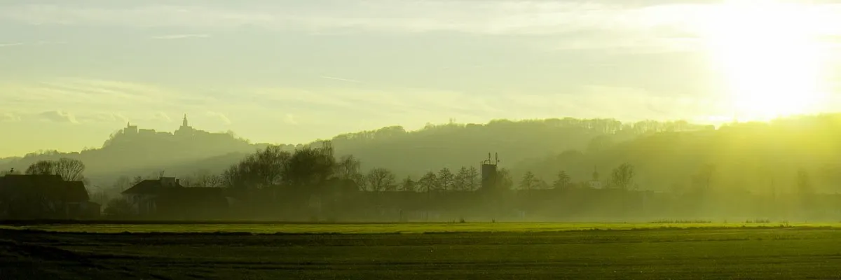 Eine friedliche Landschaft mit einem nebligen Feld, einer entfernten Stadt und einem klaren Himmel bei Morgen- oder Abenddämmerung.