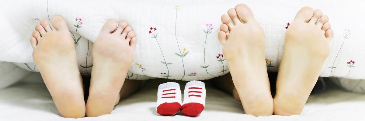 Ein Nahaufnahme von zwei Erwachsenenfüßen und einem Paar Babysocken auf einem Bett mit einer blumengemusterten Decke.