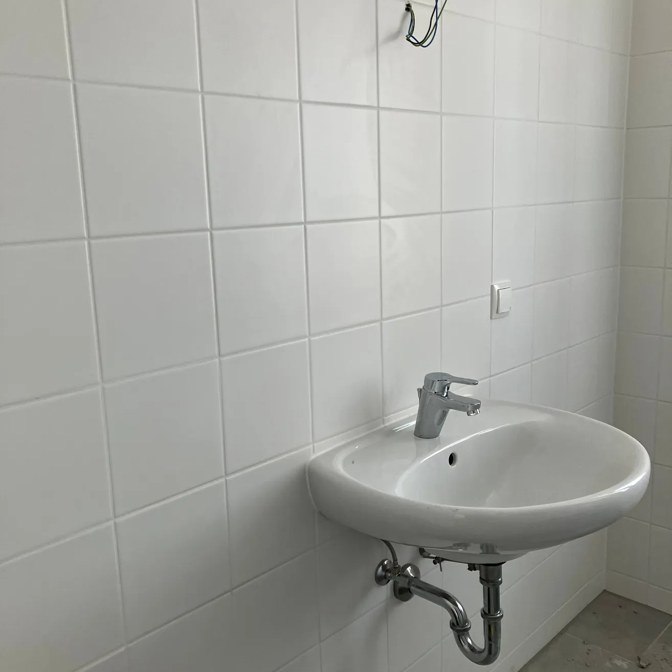 Ein Badezimmer mit weißen gefliesten Wänden und einem weißen Waschbecken mit silbernem Wasserhahn.