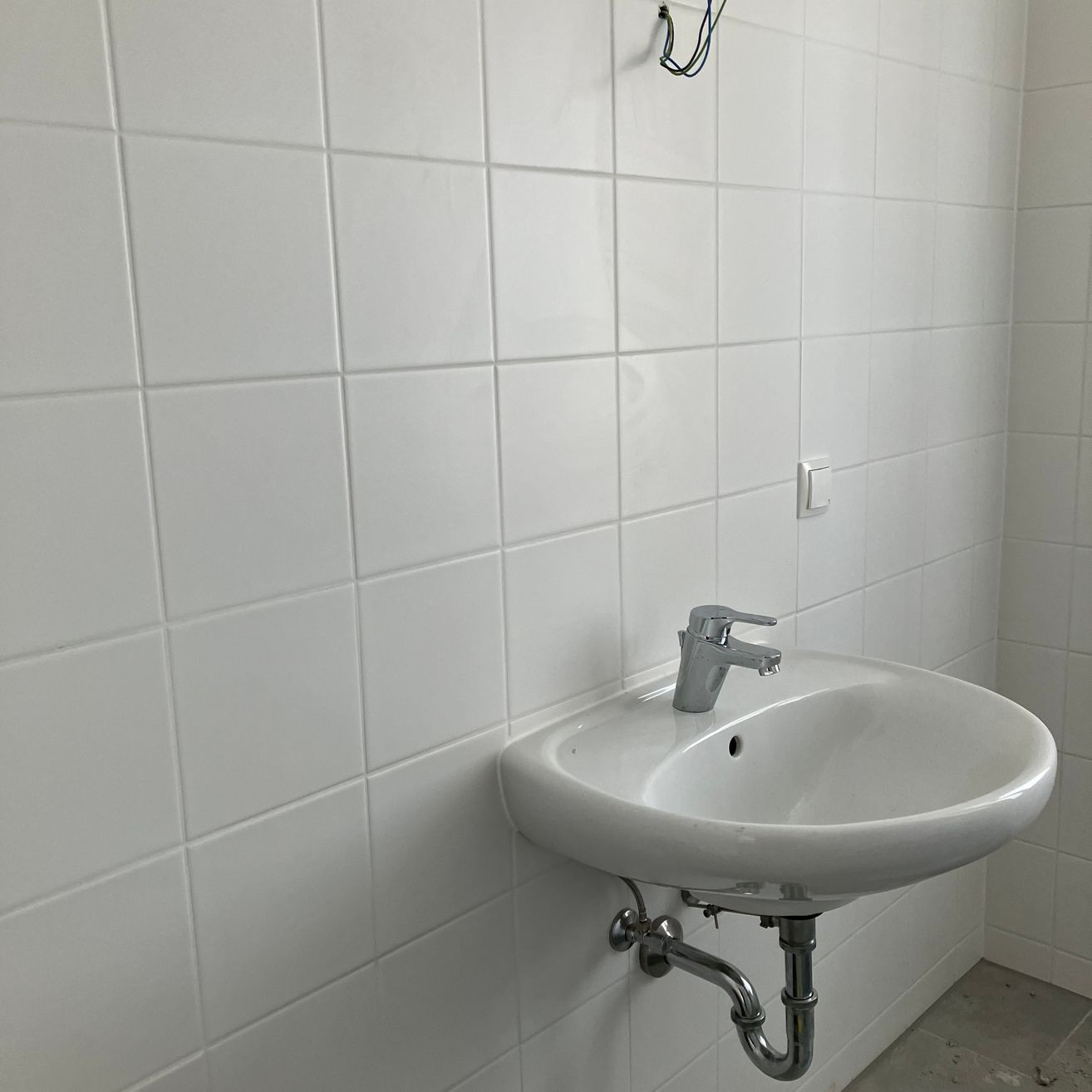 Ein Badezimmer mit weißen gefliesten Wänden und einem weißen Waschbecken mit silbernem Wasserhahn.