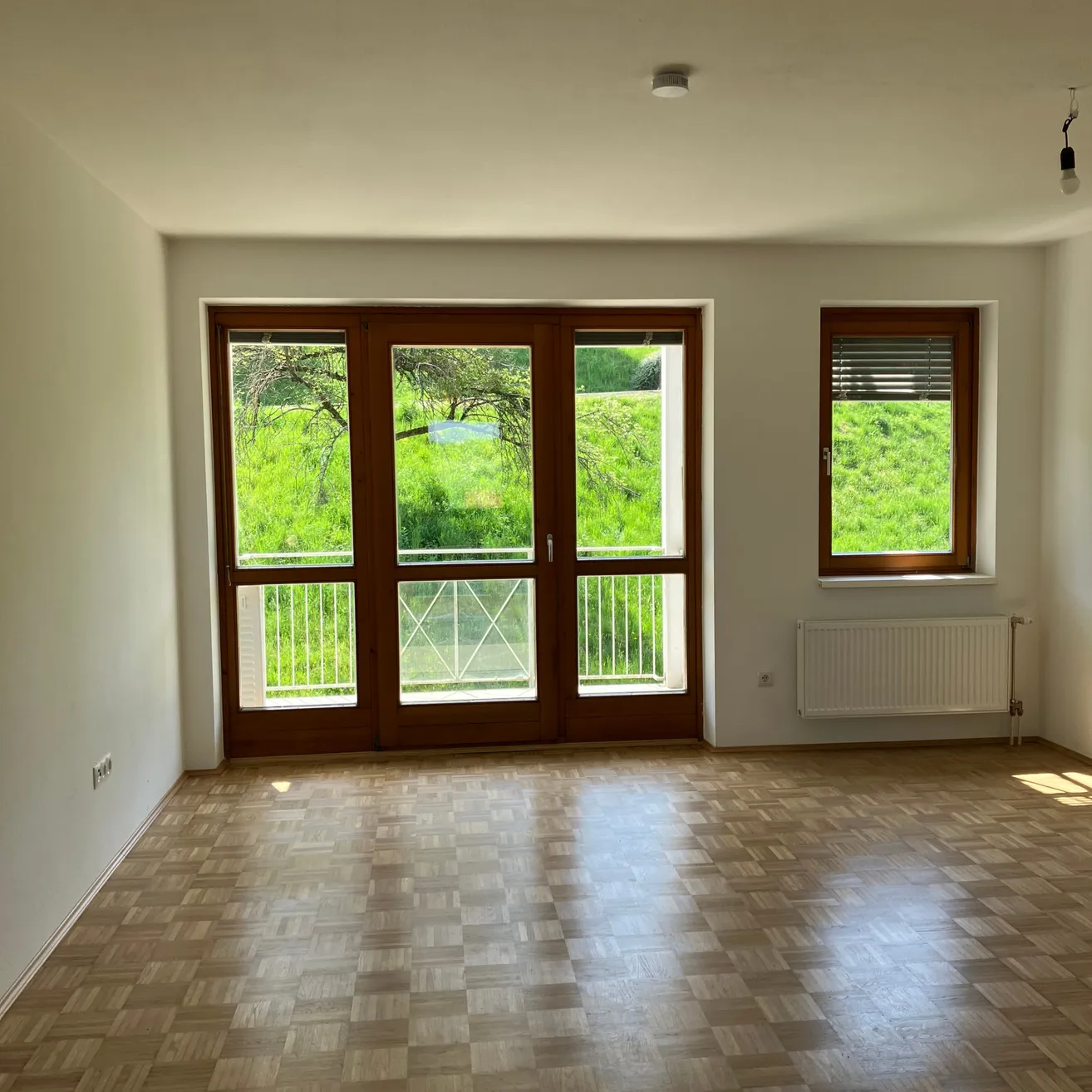 Ein leerer Raum mit Holzböden und großen Fenstern, die einen Blick auf ein grünes Feld bieten.