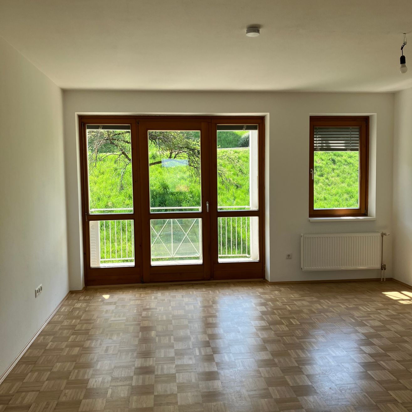 Ein leerer Raum mit Holzböden und großen Fenstern, die einen Blick auf ein grünes Feld bieten.