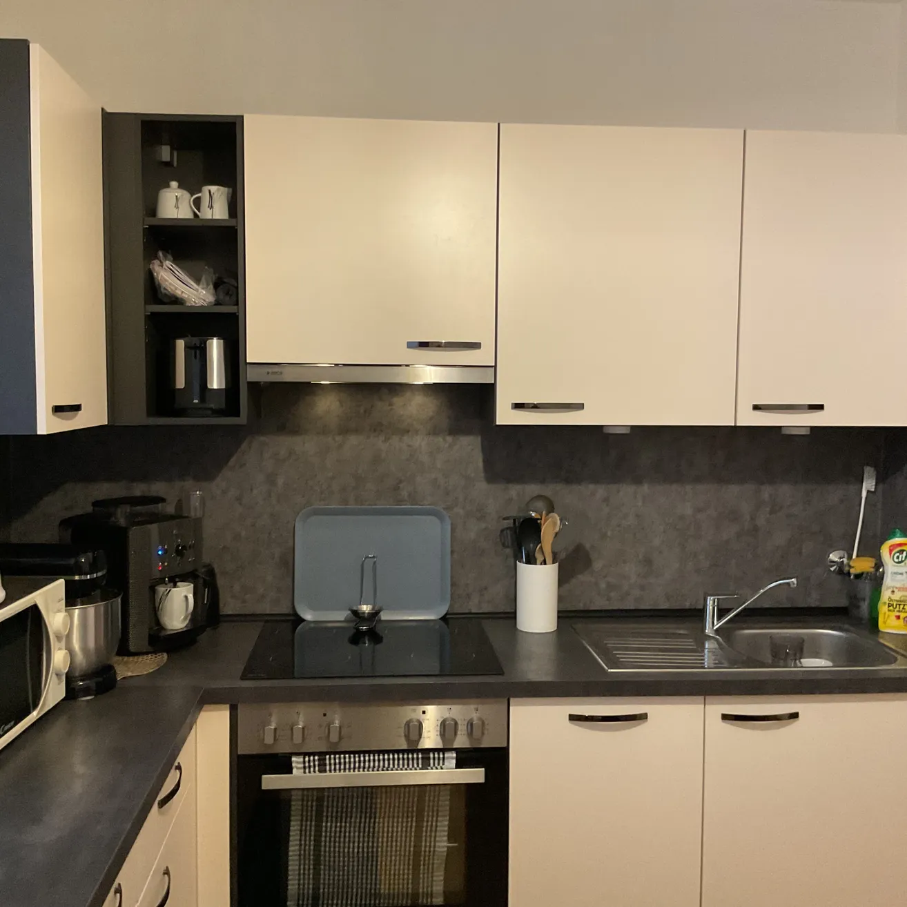 Eine moderne Küche mit weißen Schränken, grauen Arbeitsplatten und verschiedenen Küchengeräten wie Herd, Mikrowelle und Kaffeemaschine.
