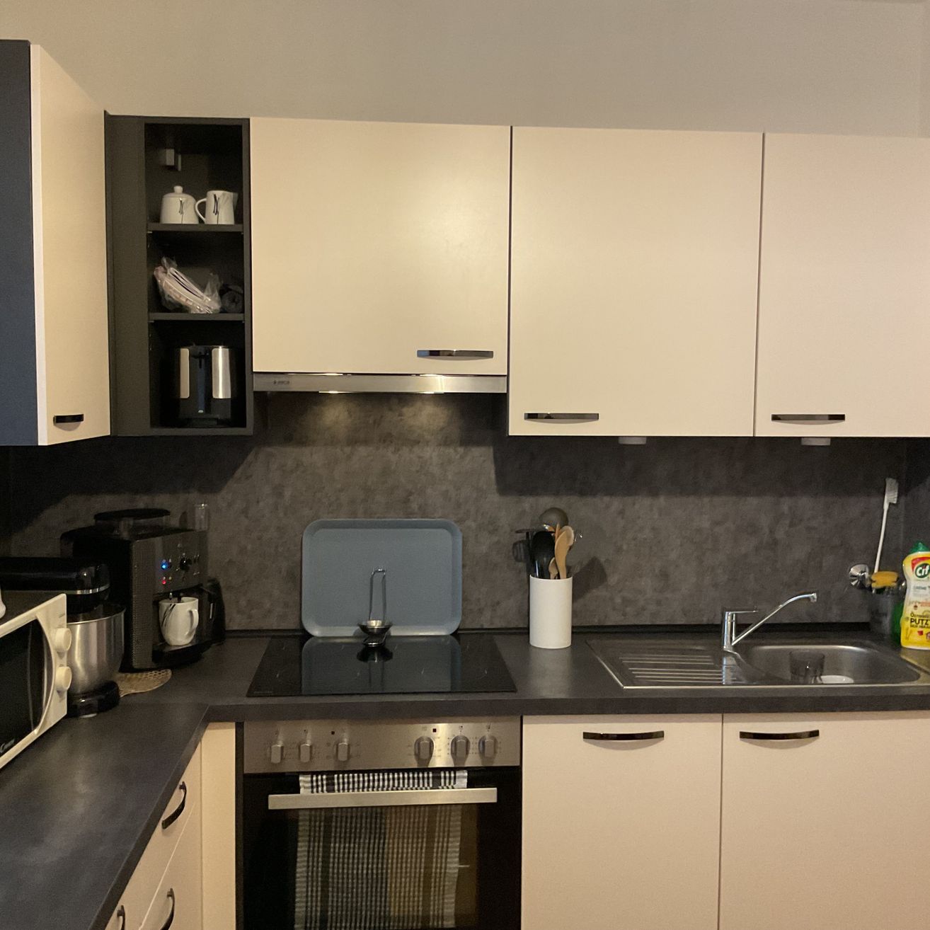 Eine moderne Küche mit weißen Schränken, grauen Arbeitsplatten und verschiedenen Küchengeräten wie Herd, Mikrowelle und Kaffeemaschine.