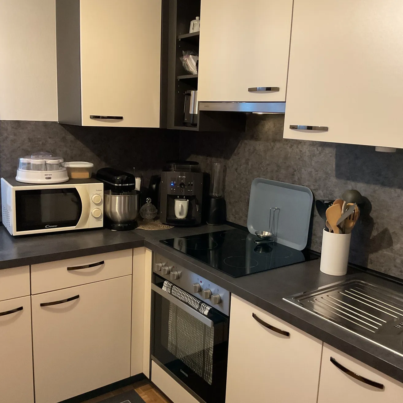 Eine moderne Küche mit weißen Schränken, einer schwarzen Arbeitsplatte und verschiedenen Küchengeräten wie Mikrowelle, Mixer und Kaffeemaschine.