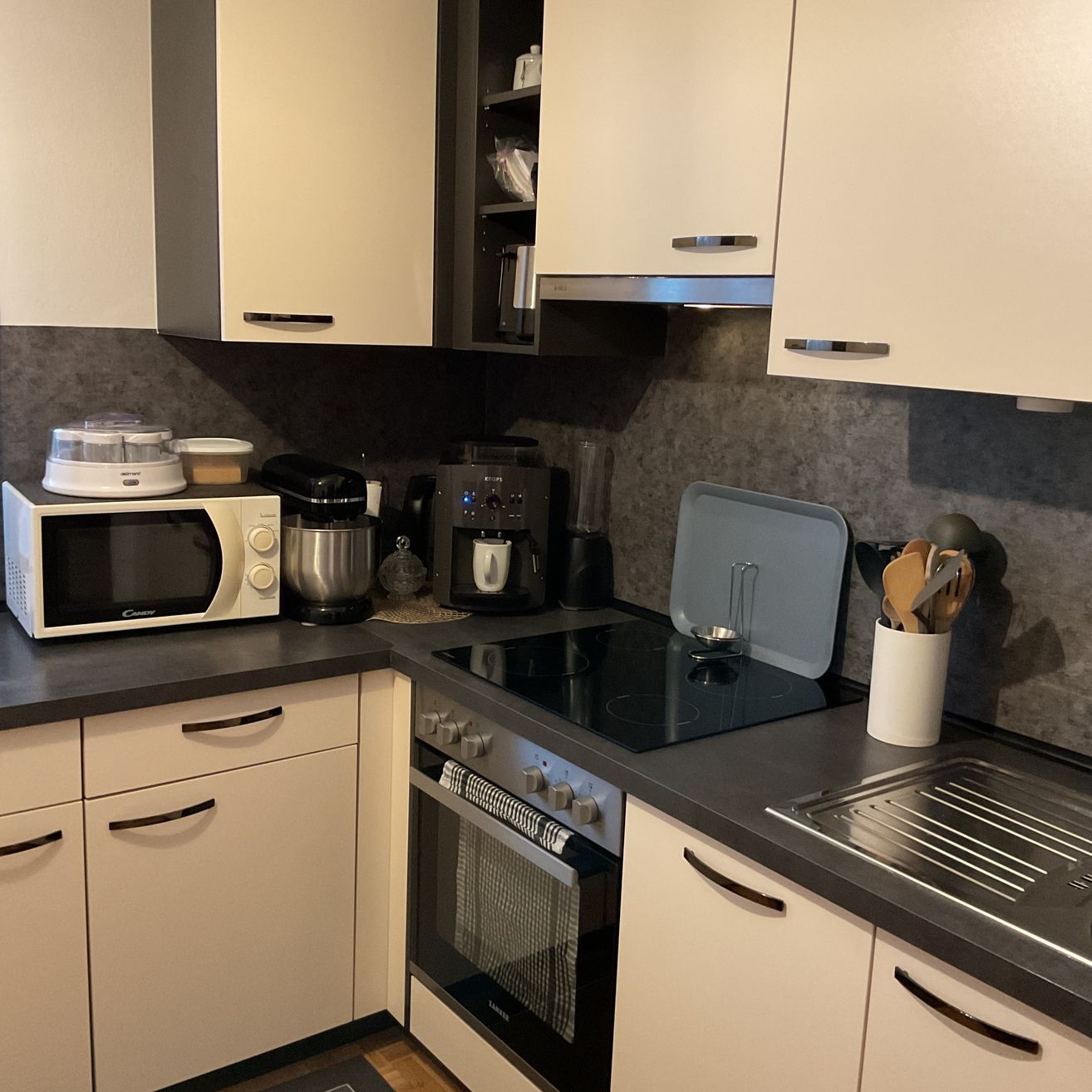 Eine moderne Küche mit weißen Schränken, einer schwarzen Arbeitsplatte und verschiedenen Küchengeräten wie Mikrowelle, Mixer und Kaffeemaschine.
