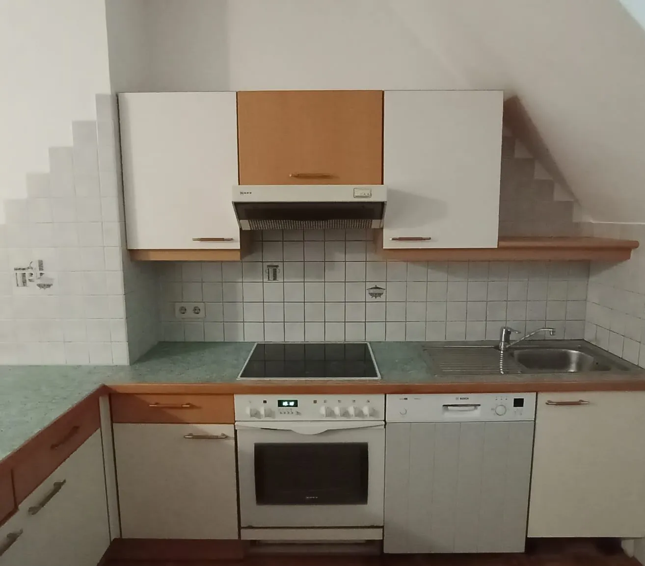 Eine Küche mit weißen Schränken, einer grünen Arbeitsplatte, einem Herd, einem Waschbecken und einer Spülmaschine. Die Wand ist mit weißen Fliesen verkleidet.