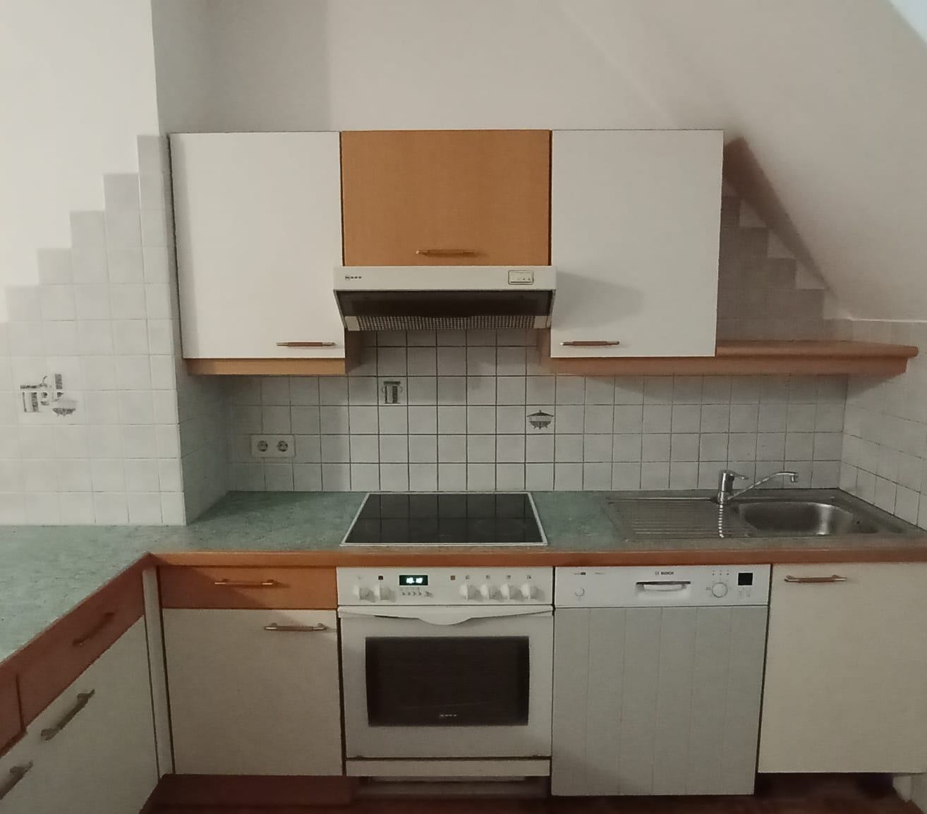 Eine Küche mit weißen Schränken, einer grünen Arbeitsplatte, einem Herd, einem Waschbecken und einer Spülmaschine. Die Wand ist mit weißen Fliesen verkleidet.