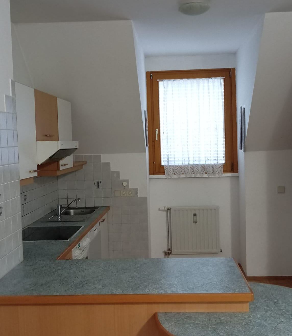 Eine kleine Küche mit einem Waschbecken, einem Fenster mit weißen Vorhängen und einem Holzschrank.