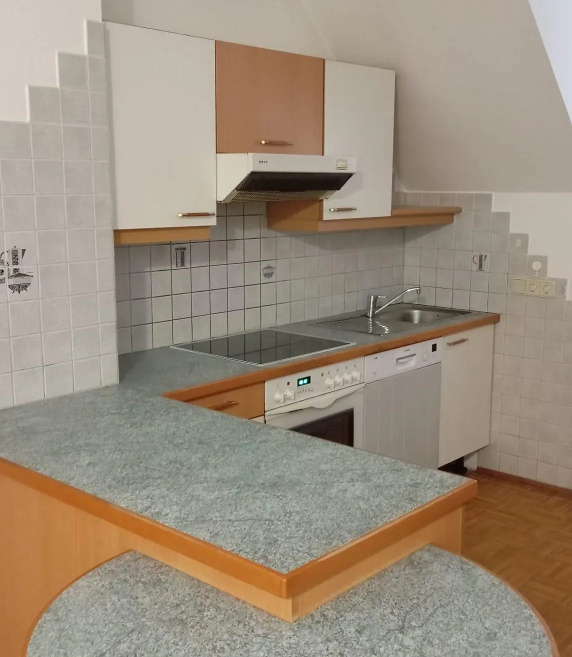 Eine moderne Küche mit weißen Schränken, Granitarbeitsplatten, einem Gasherd und einer Spülmaschine. Die Wände sind gefliest und rechts befindet sich eine Steckdose.