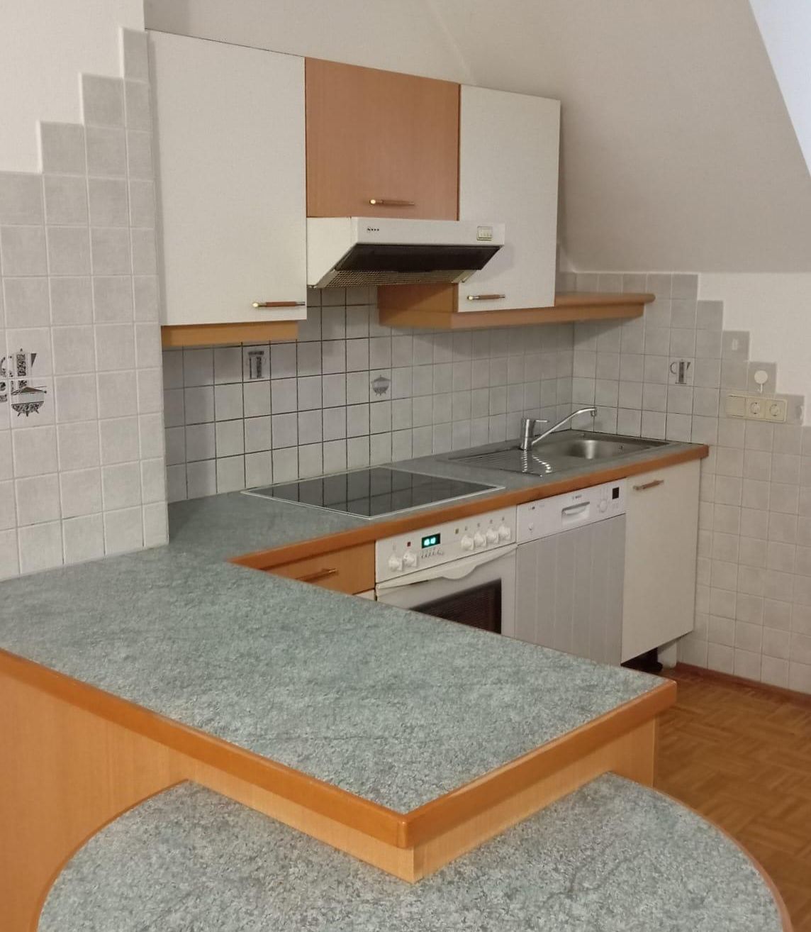 Eine moderne Küche mit weißen Schränken, Granitarbeitsplatten, einem Gasherd und einer Spülmaschine. Die Wände sind gefliest und rechts befindet sich eine Steckdose.