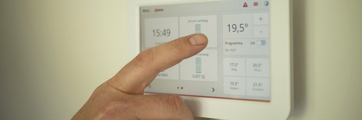 Eine Hand drückt einen Knopf auf einem digitalen Thermostaten, der die Zeit als 15:49 und die Temperatur als 19,5 Grad Celsius anzeigt.