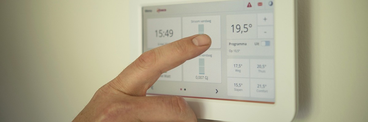 Eine Hand drückt einen Knopf auf einem digitalen Thermostaten, der die Zeit als 15:49 und die Temperatur als 19,5 Grad Celsius anzeigt.