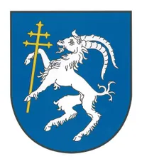 Ein blauer Schild mit einem weißen Widder, der einen goldenen Kreuz in seinem Maul hält und auf einem Bein steht.