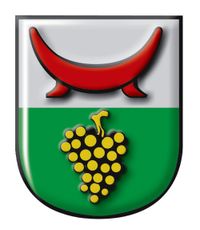 Ein schildförmiges Emblem mit einem roten Halbmond oben und einem Strauß gelber und schwarzer Trauben in der Mitte auf grünem Hintergrund.