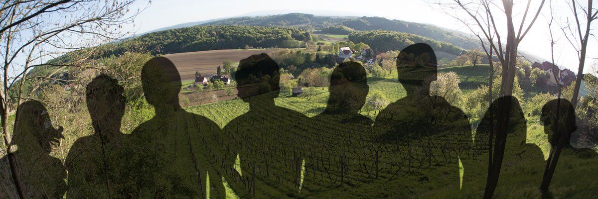 Die Silhouette von vier Personen in einem üppigen grünen Feld mit Blick auf ein Dorf und Berge in der Ferne.