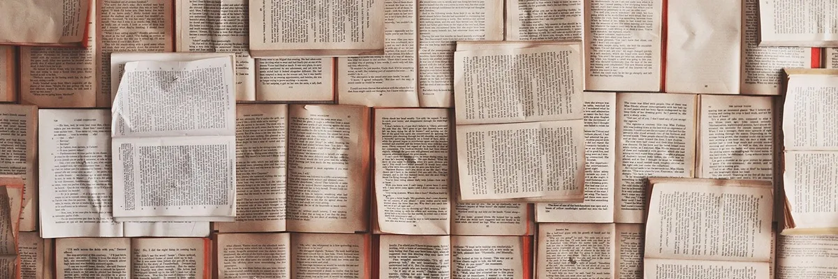 Eine Nahaufnahme von mehreren Büchern, die aufeinandergestapelt sind und Seiten mit Text sowie einige mit leeren Stellen zeigen. Die Bücher sind in verschiedenen Größen und Farben, einige erscheinen alt und abgenutzt.