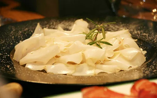 Ein Teller mit cremiger Pasta und einem Rosmarinzweig als Garnierung. Die Pasta ist mit einer Tomatenscheibe garniert.