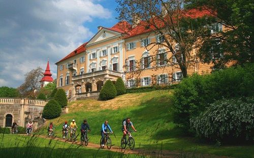 Eine Gruppe von Radfahrern fährt auf einem Pfad vor einem großen, kunstvollen Gebäude mit rotem Dach.