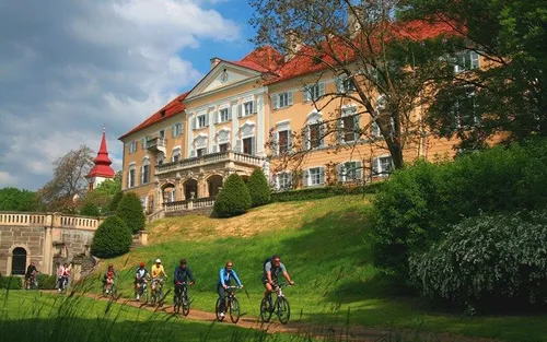 Eine Gruppe von Radfahrern fährt auf einem Pfad vor einem großen, kunstvollen Gebäude mit rotem Dach.