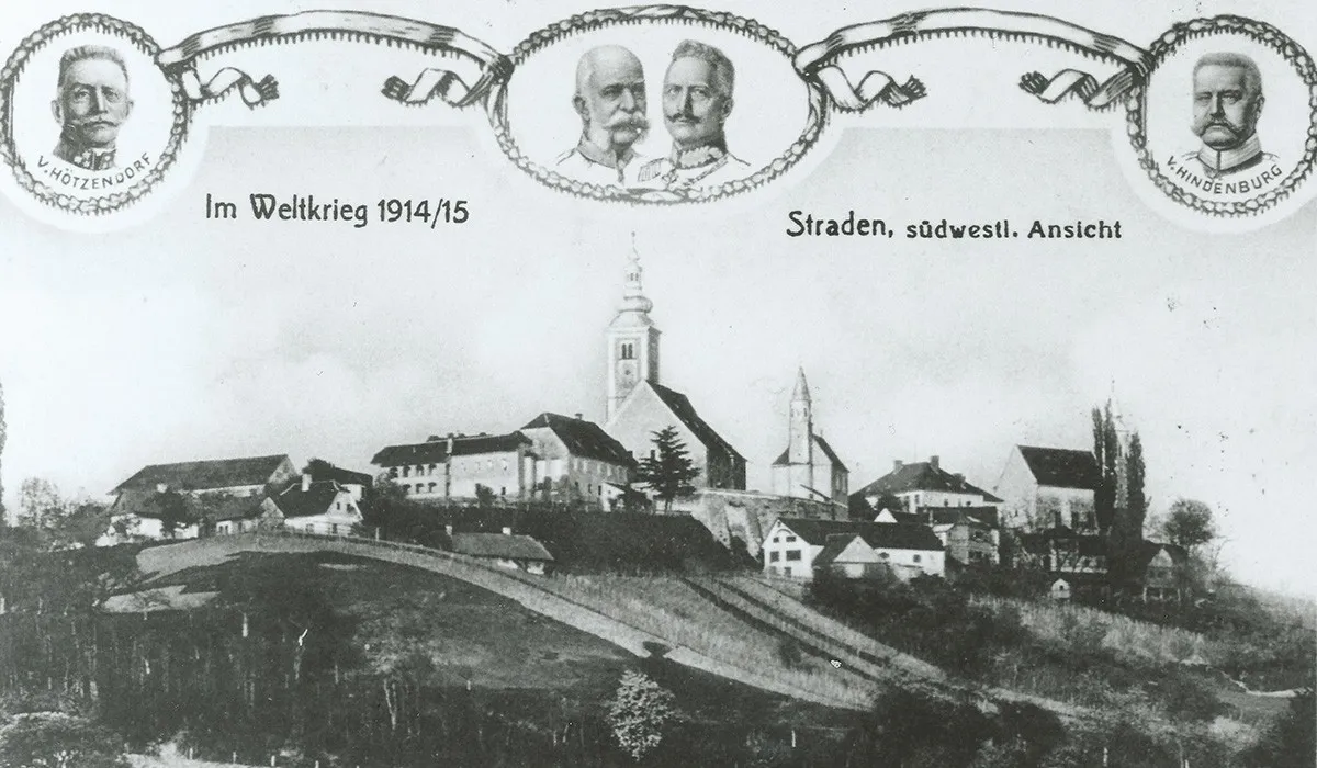 Ein Schwarz-Weiß-Foto aus dem Ersten Weltkrieg, das eine Stadt mit einer Kirche und einer Burg zeigt. Über dem Bild sind zwei Männer abgebildet mit dem Text 'Weltkrieg 1914/15'.