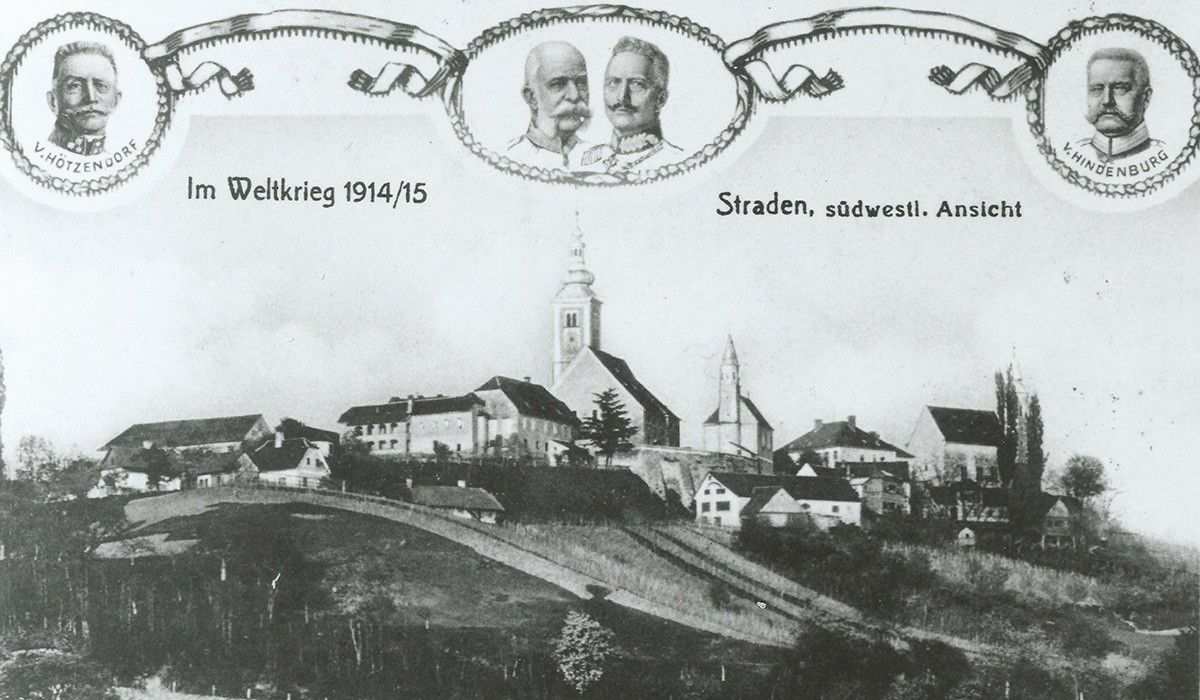 Ein Schwarz-Weiß-Foto aus dem Ersten Weltkrieg, das eine Stadt mit einer Kirche und einer Burg zeigt. Über dem Bild sind zwei Männer abgebildet mit dem Text 'Weltkrieg 1914/15'.