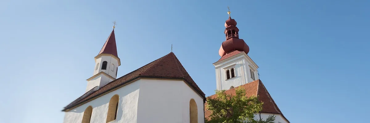 Eine Kirche mit zwei Türmen, einer mit einer roten Kuppel und der andere mit einem spitzen Dach. Die Kirche hat ein braunes Dach und weiße Wände mit Bogenfenstern.