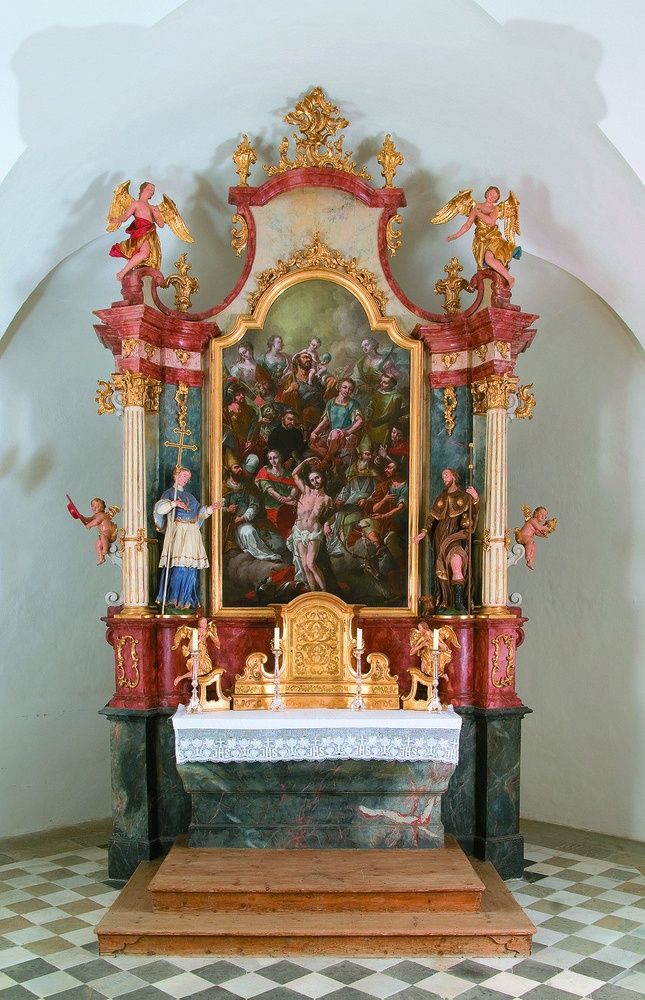 Ein kunstvoller Altaraufsatz in einer Kirche zeigt ein zentrales Gemälde von Jesus Christus, umgeben von Engeln und Figuren, flankiert von Statuen und dekorativen Elementen.