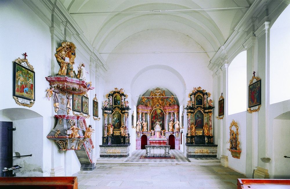 Ein Innenraum einer Kirche mit kunstvollen Altären und Statuen, mit einem zentralen Altar mit einem Gemälde und einem Seitenaltar mit einer Statue von Jesus Christus.