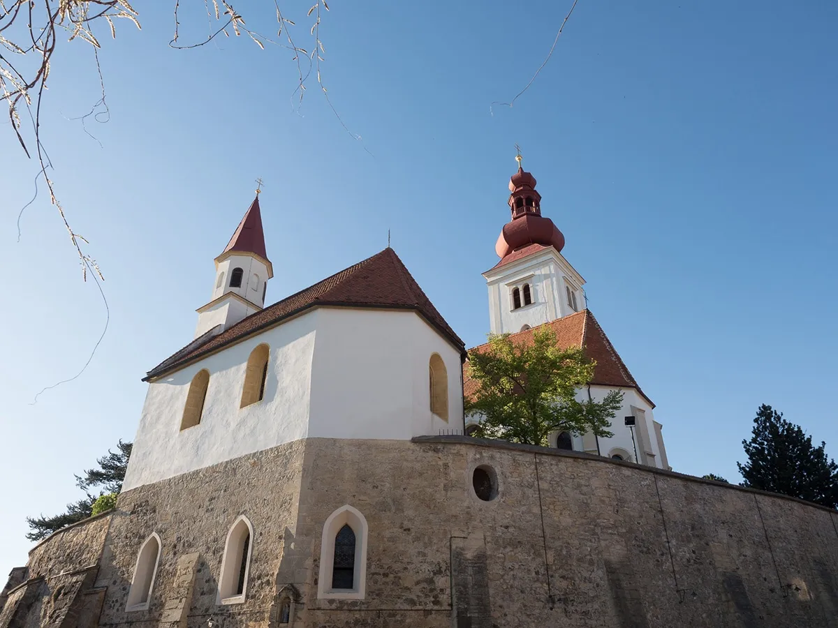Eine Kirche mit zwei Türmen, einer mit einem roten Dach und der andere mit einem weißen Dach. Die Kirche ist weiß gestrichen und hat ein braunes Dach.